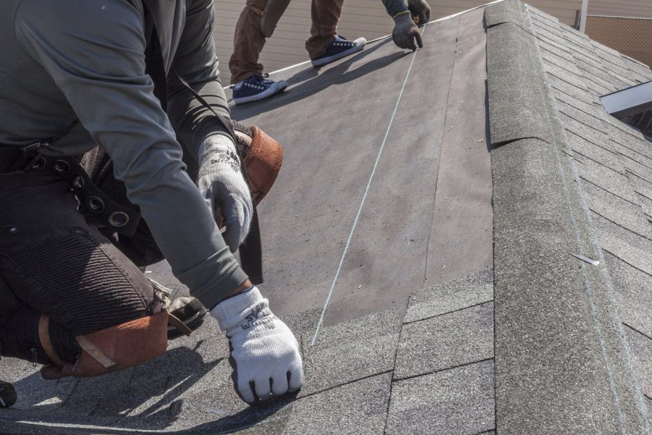 Two roofers snapping a chalk line on underlayment beside freshly installed gray asphalt shingles