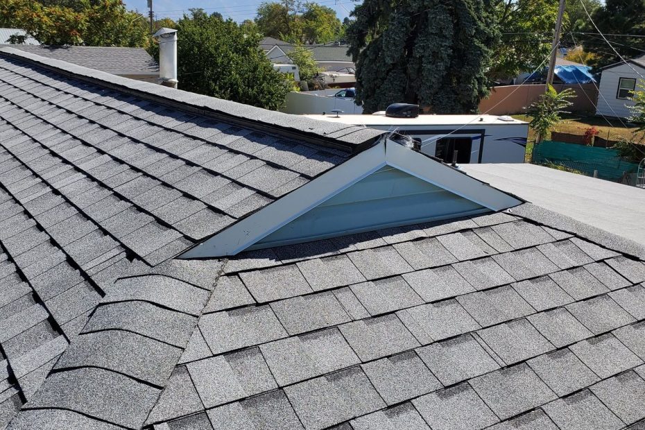 New gray asphalt shingle roof with ridge, hip and valley beside a white triangular dormer; mountains behind