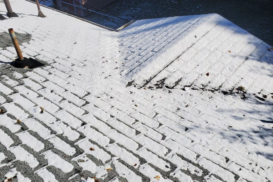 Light snow on asphalt shingle roof with pipe boot, hip line, and backyard shed below