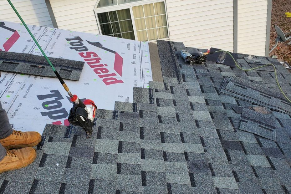 Steep roof mid-shingling: gray shingles, white Top Shield underlayment, two nail guns, worker's boots at edge