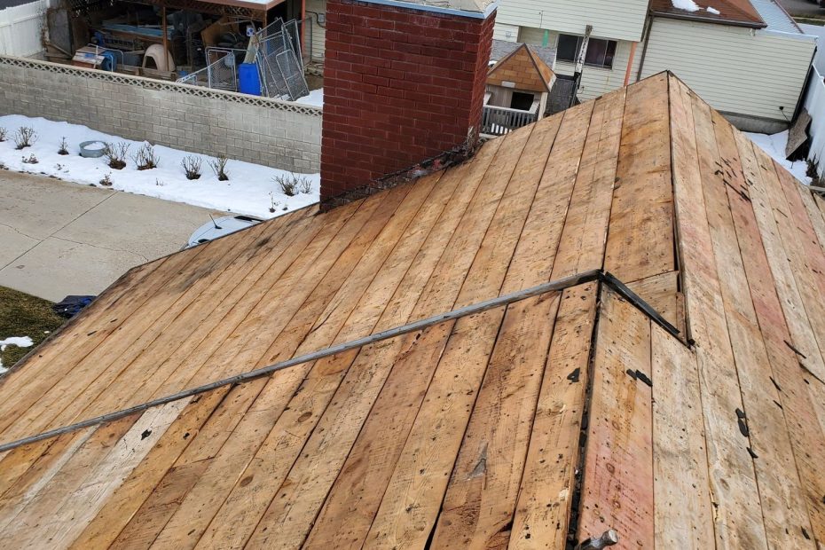 Roof torn off to bare wood plank decking, hammer on slope, brick chimney and snowy neighborhood behind