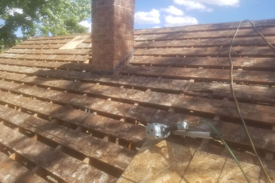 Roof torn off to spaced board decking beside a brick chimney, new OSB sheathing and nail gun nearby