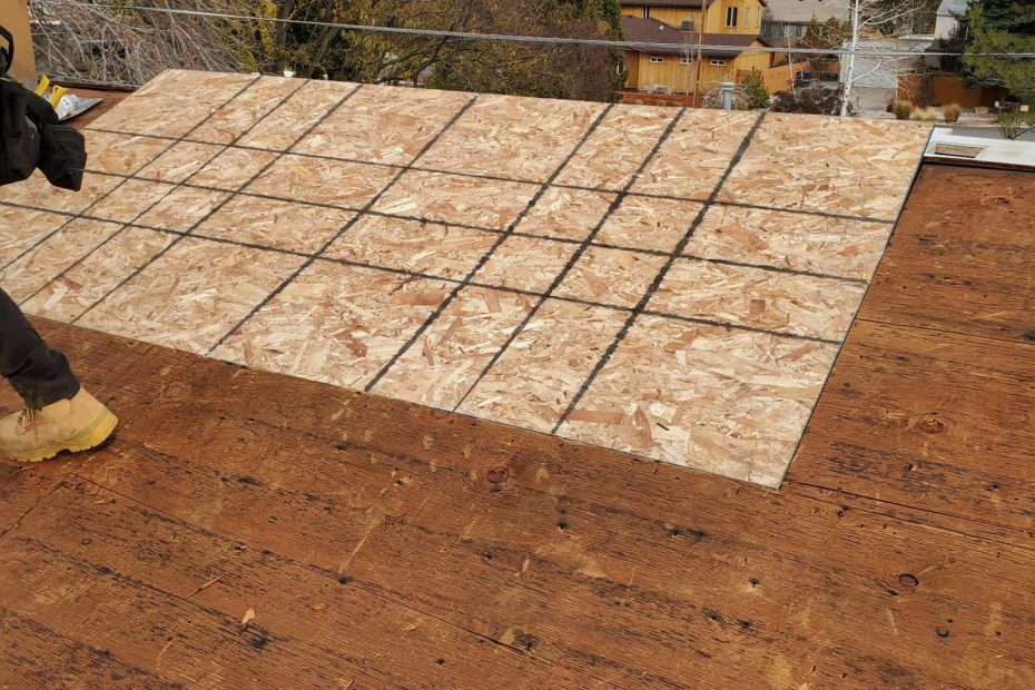 Stripped roof deck of old planks partly re-sheathed with new OSB panels, worker's boot at left edge