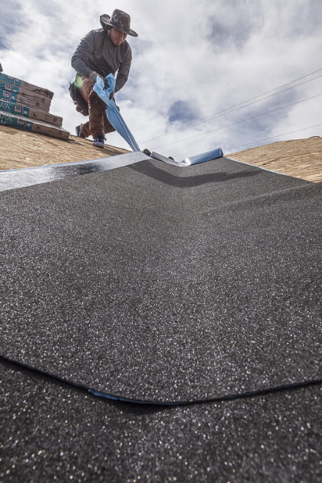 A Hancock roofer rolling self-adhering ice barrier down a valley on new decking before the shingles go on