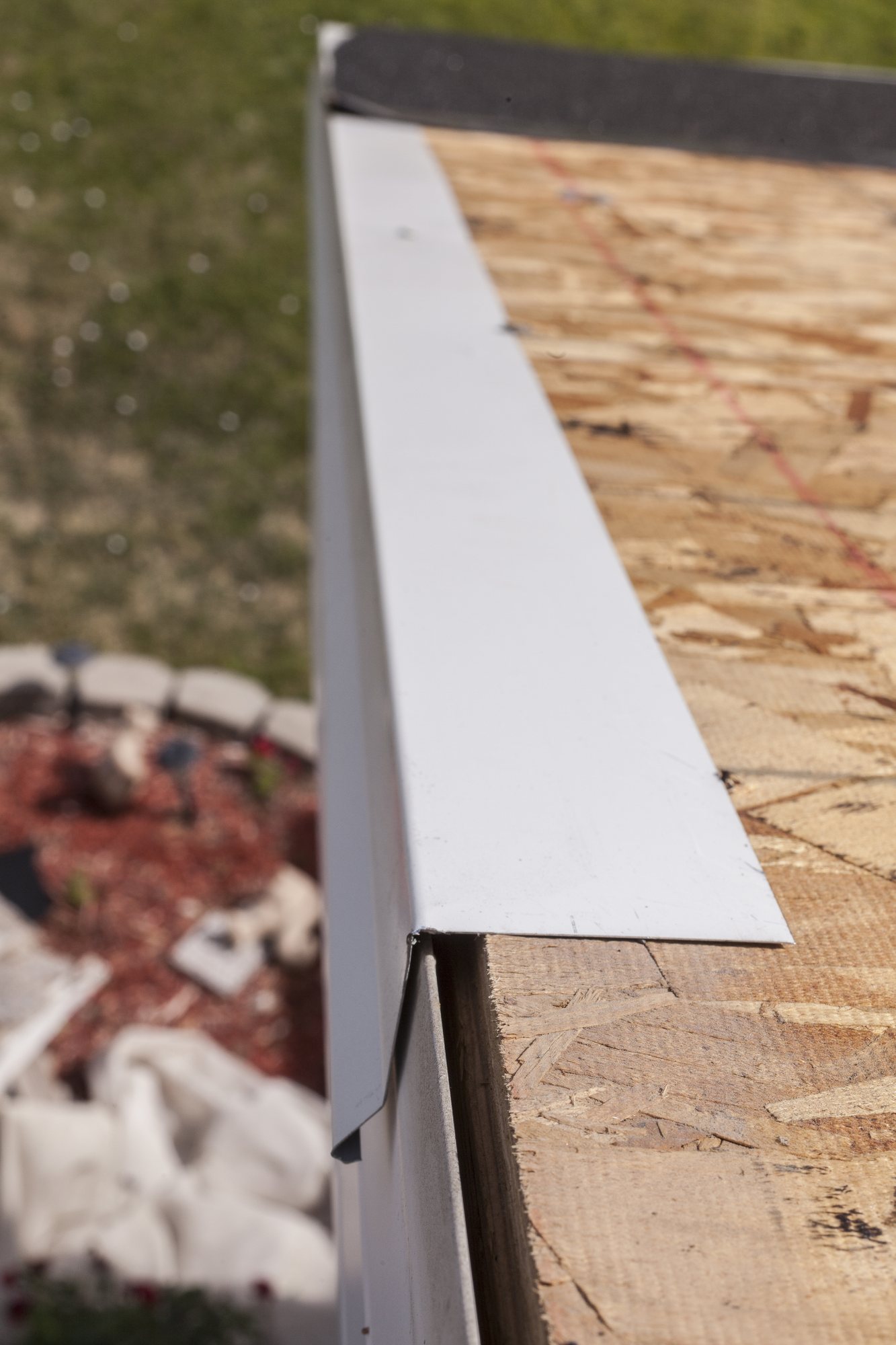 White metal drip edge along a roof eave over bare OSB decking, lawn below
