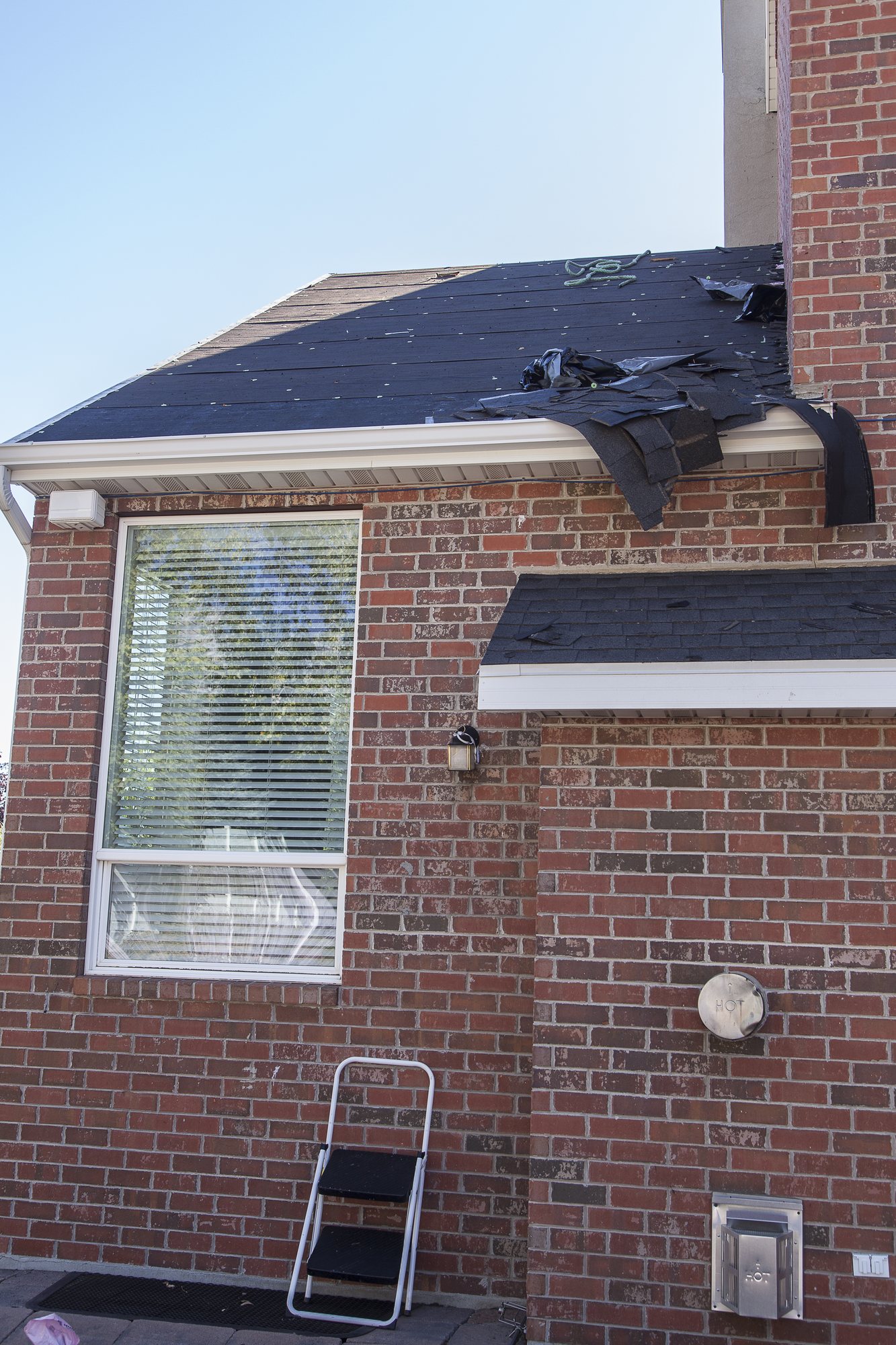 Brick house with roof stripped to black underlayment, torn material draped over the white gutter, in South Jordan, UT