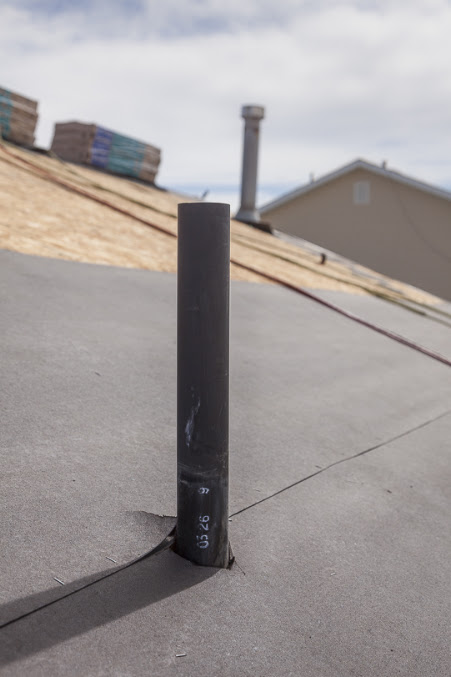 Black vent pipe through gray roof underlayment; bare decking and stacked shingle bundles beyond, in Murray, UT