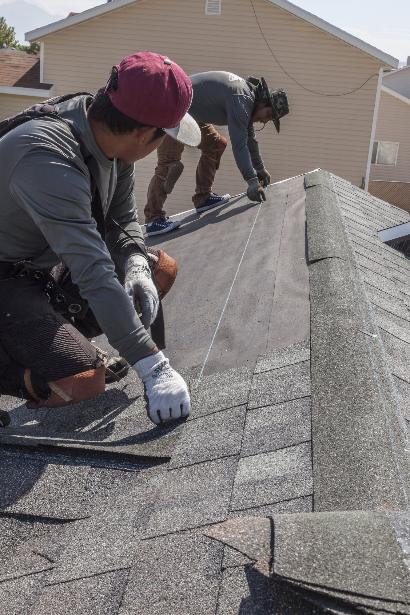 Two roofers snapping a chalk line on underlayment beside freshly installed gray asphalt shingles