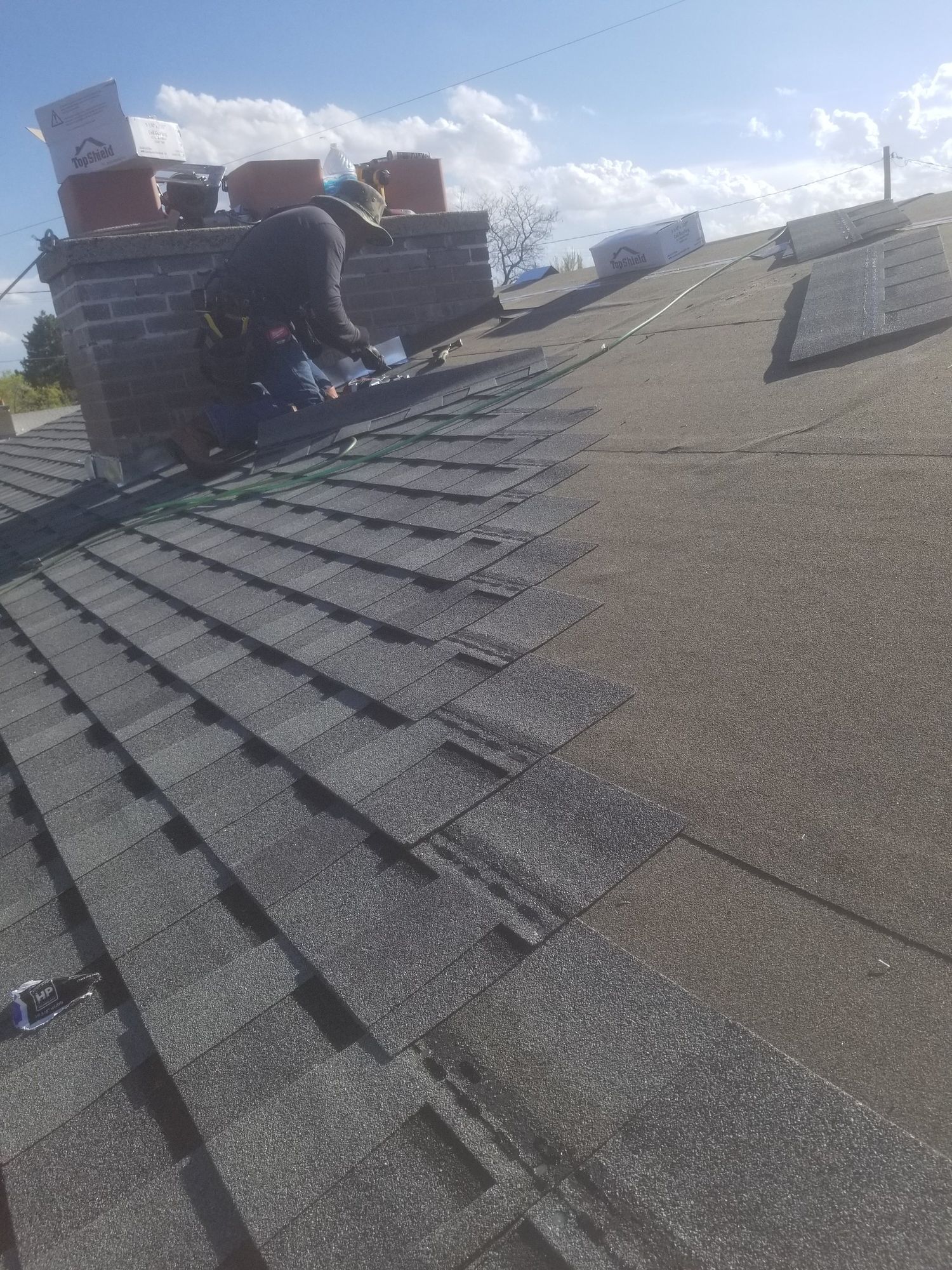 Roofer at brick chimney installing flashing as new asphalt shingles are laid over gray underlayment