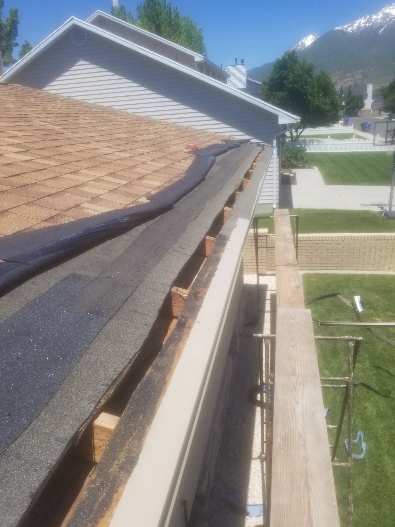 Shingle roof edge opened at the eave, exposing rafter tails and dark fascia board behind a white gutter, in Riverton, UT