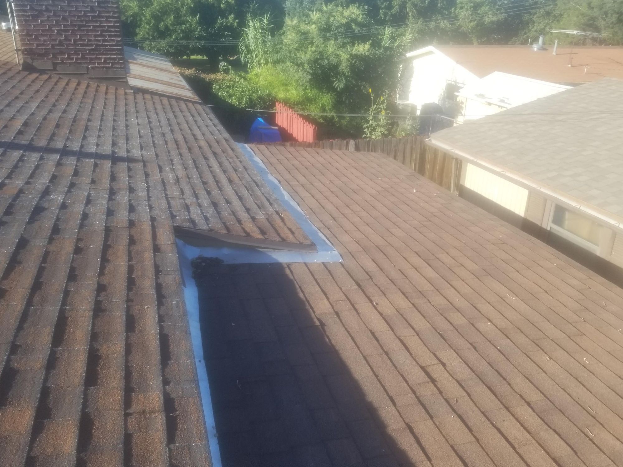 Brown shingle roof planes meeting at an open metal valley with a lifted torn strip and loose debris