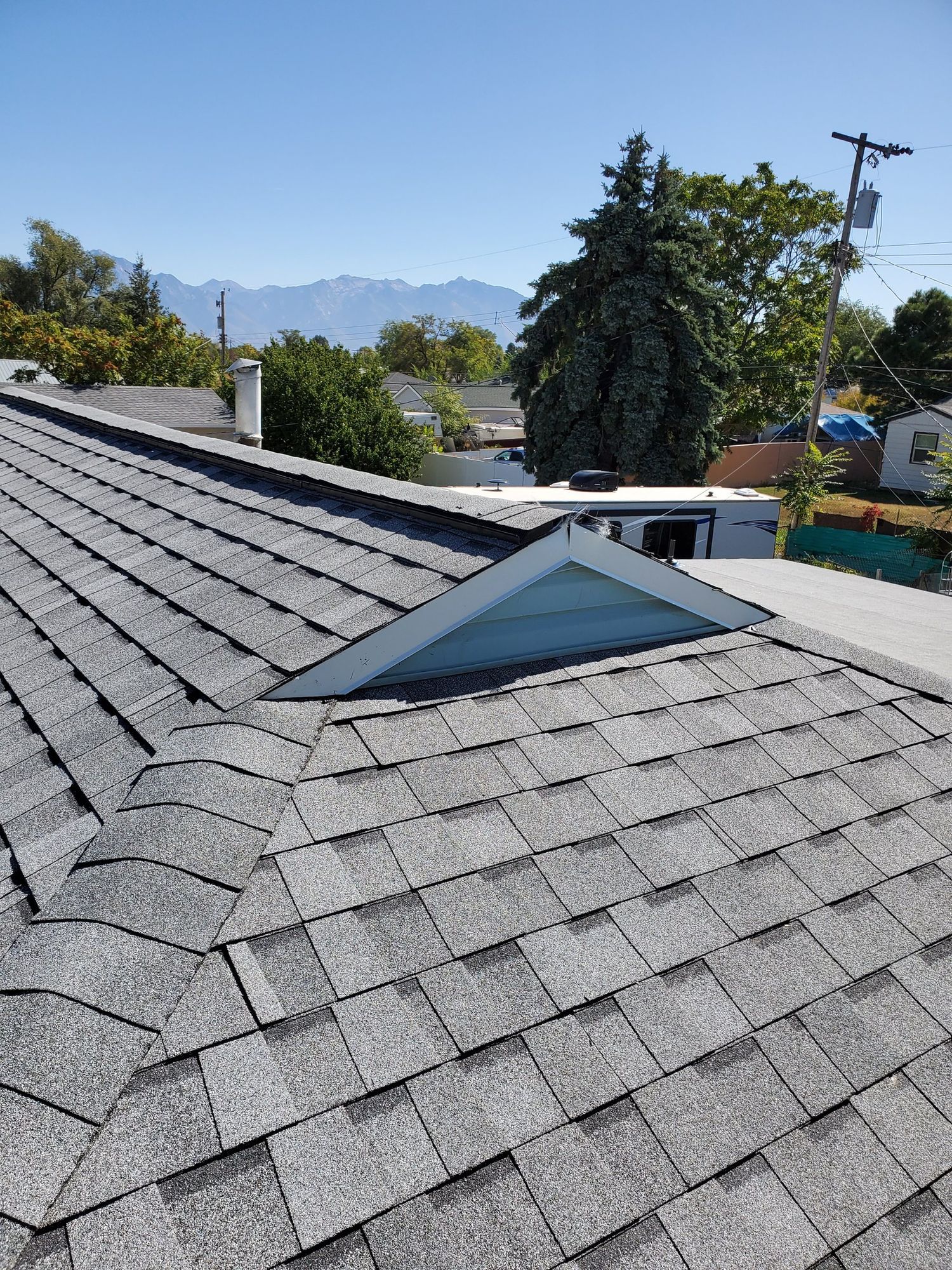 New gray asphalt shingle roof with ridge, hip and valley beside a white triangular dormer; mountains behind, in Peoa, UT