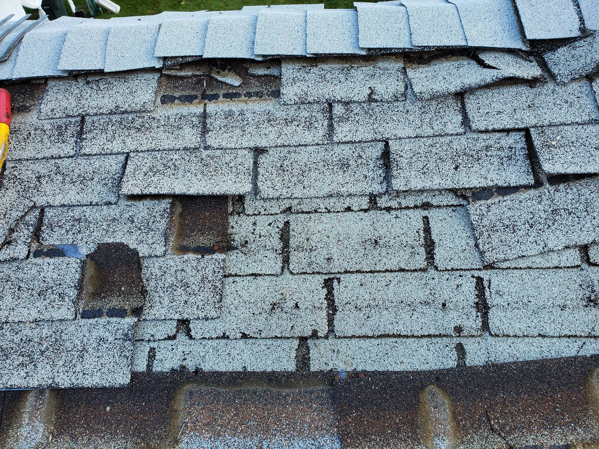 Damaged gray asphalt shingle roof near ridge with slipped and missing tabs exposing brown layers beneath, in Draper, UT
