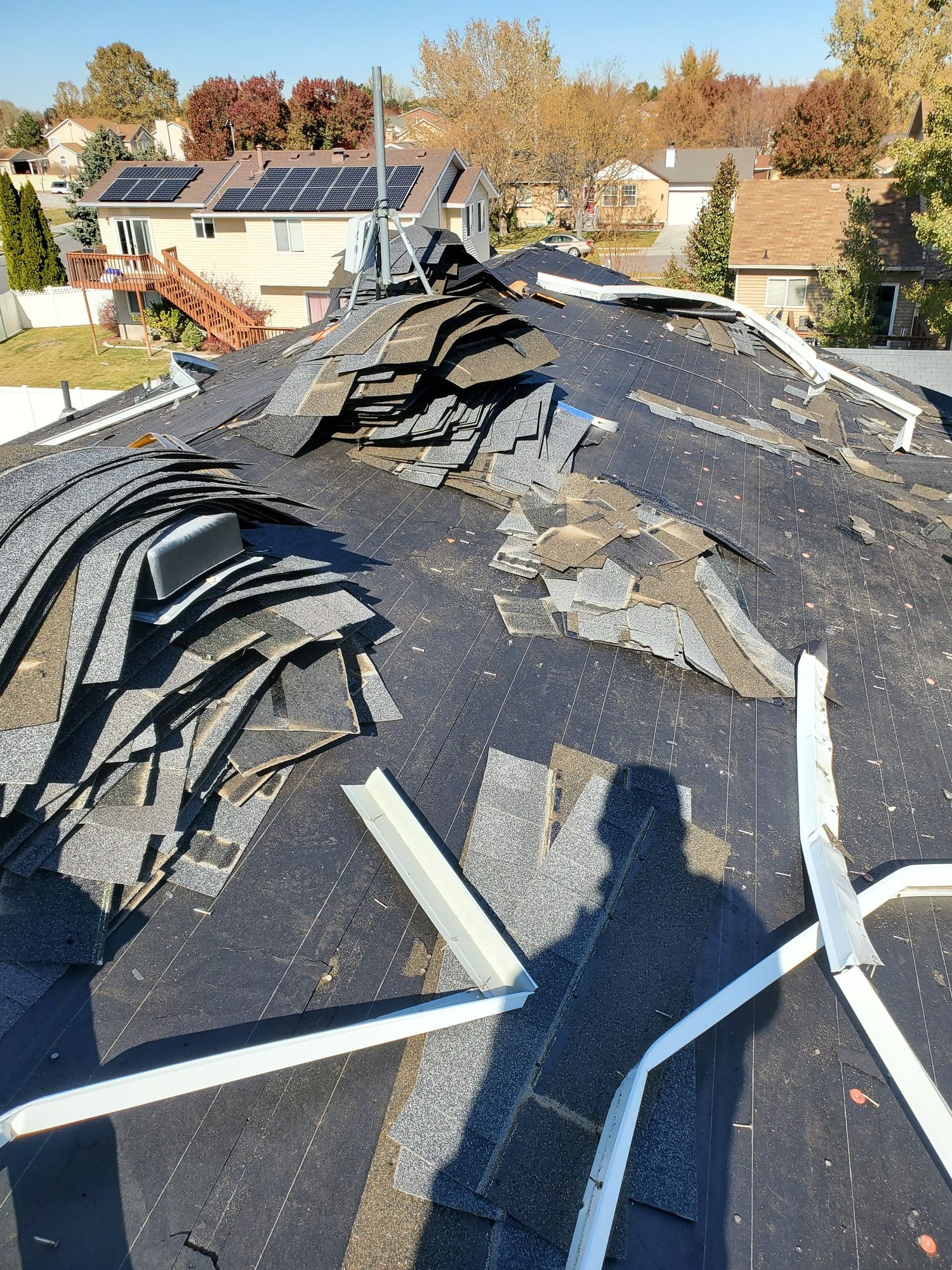 Roof tear-off: piles of old asphalt shingles on black underlayment with white drip edge pieces staged