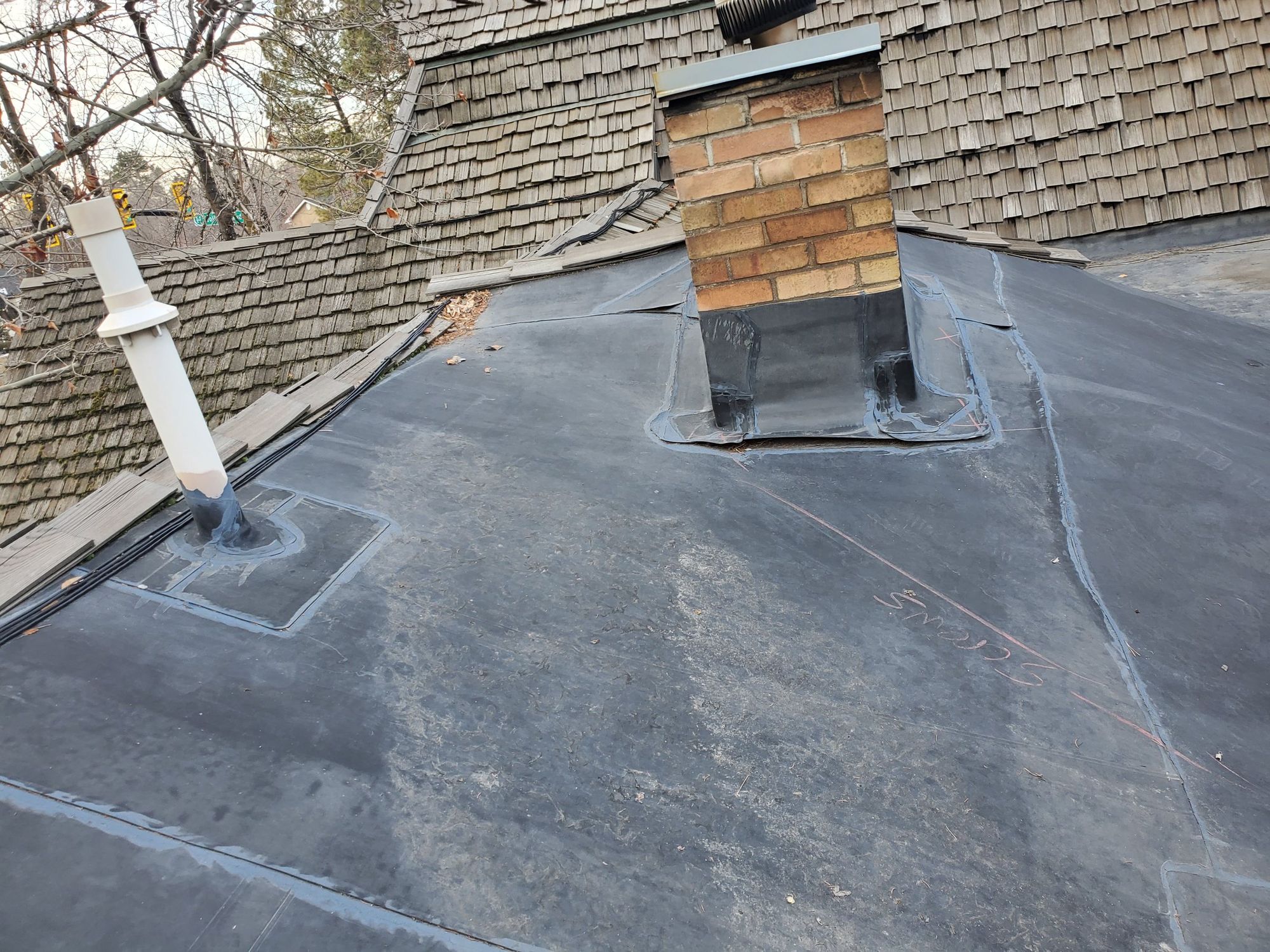 Black membrane flat roof with flashed brick chimney and vent pipe beside weathered cedar shake slopes