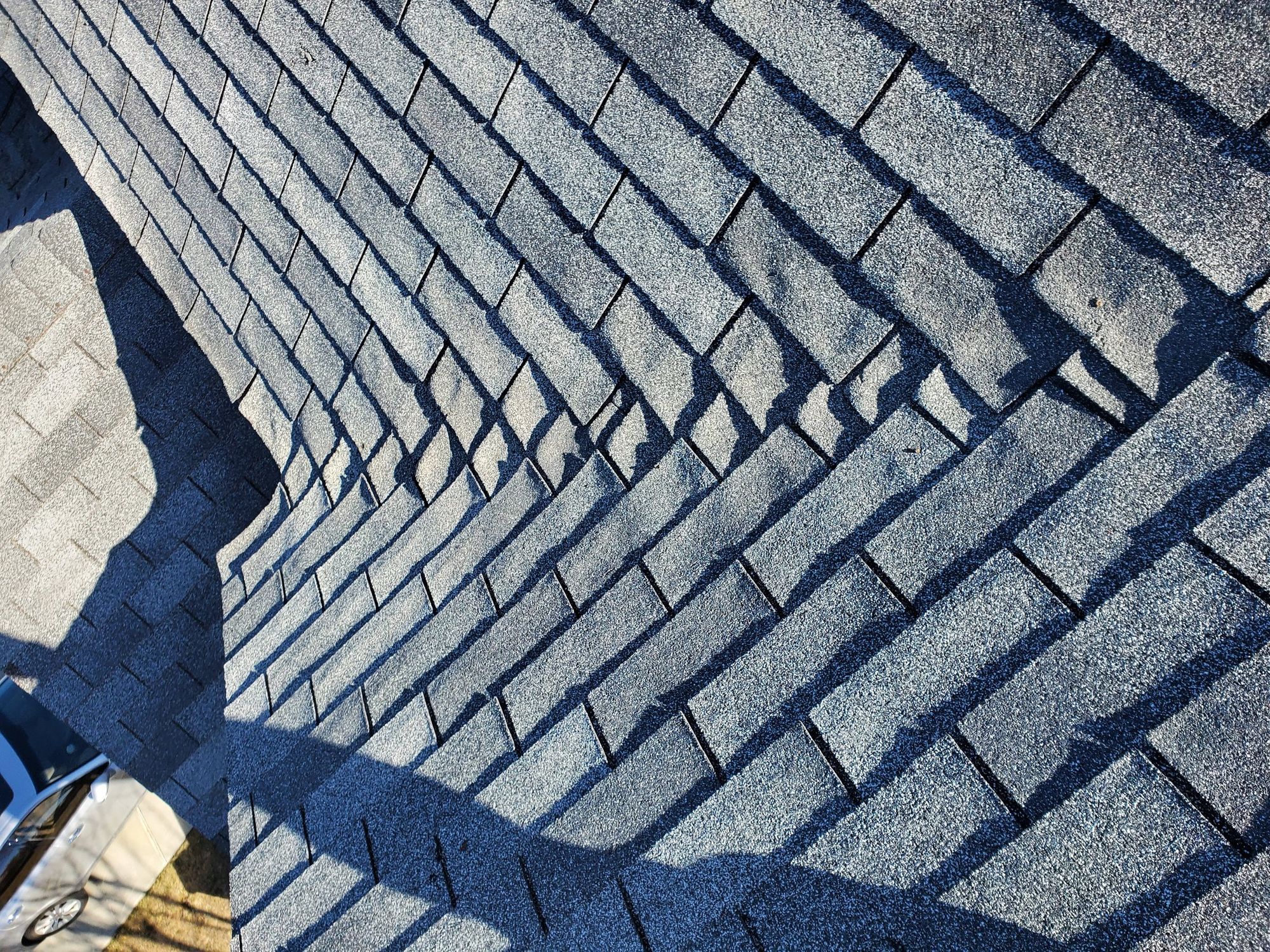 Gray asphalt shingle roof seen from above, tabs lifted and curled along a hip line, in Bountiful, UT