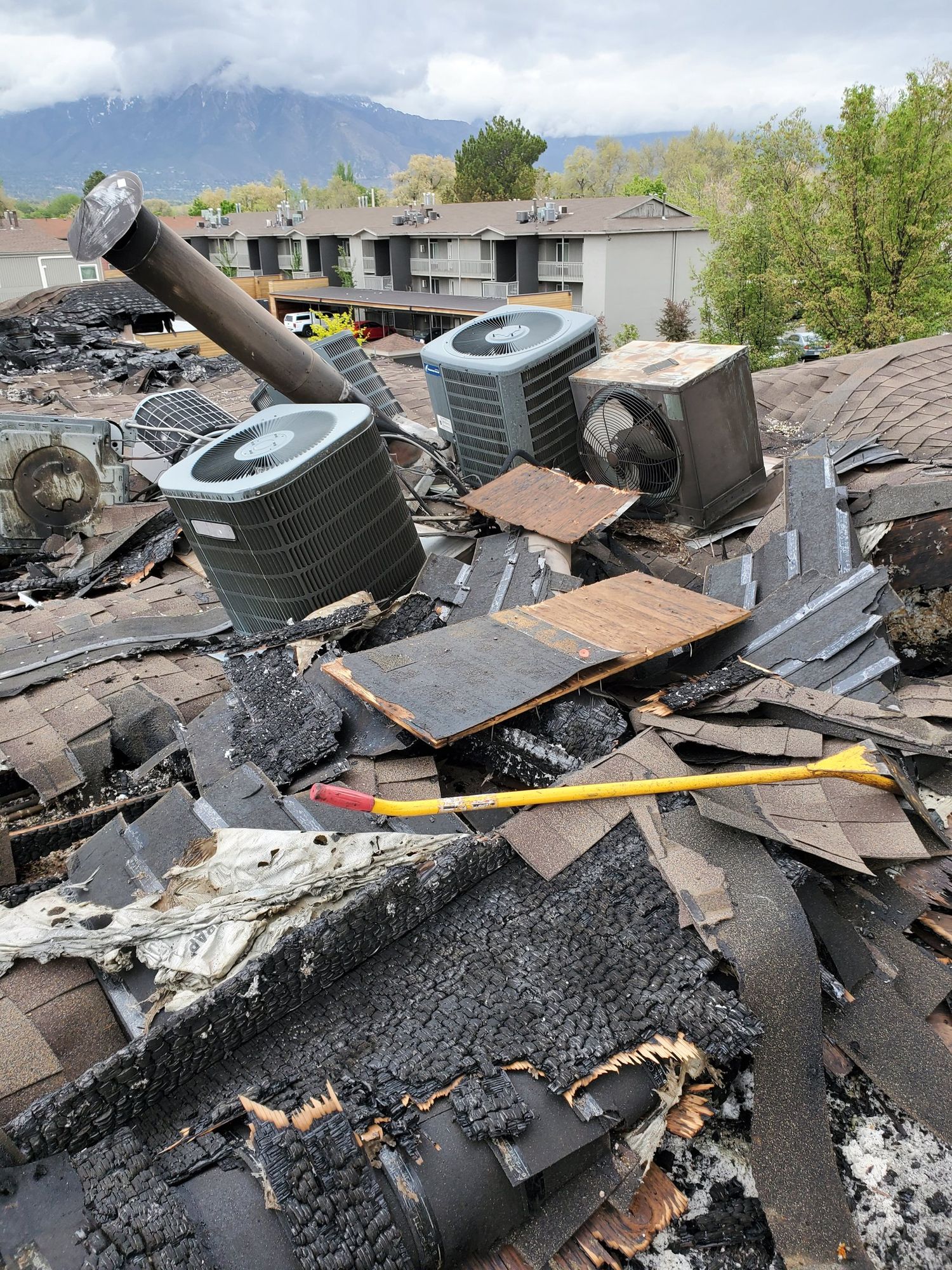 Burned asphalt shingle roof covered in charred debris, an axe, fallen flue pipe and air conditioning units, in Farmington, UT