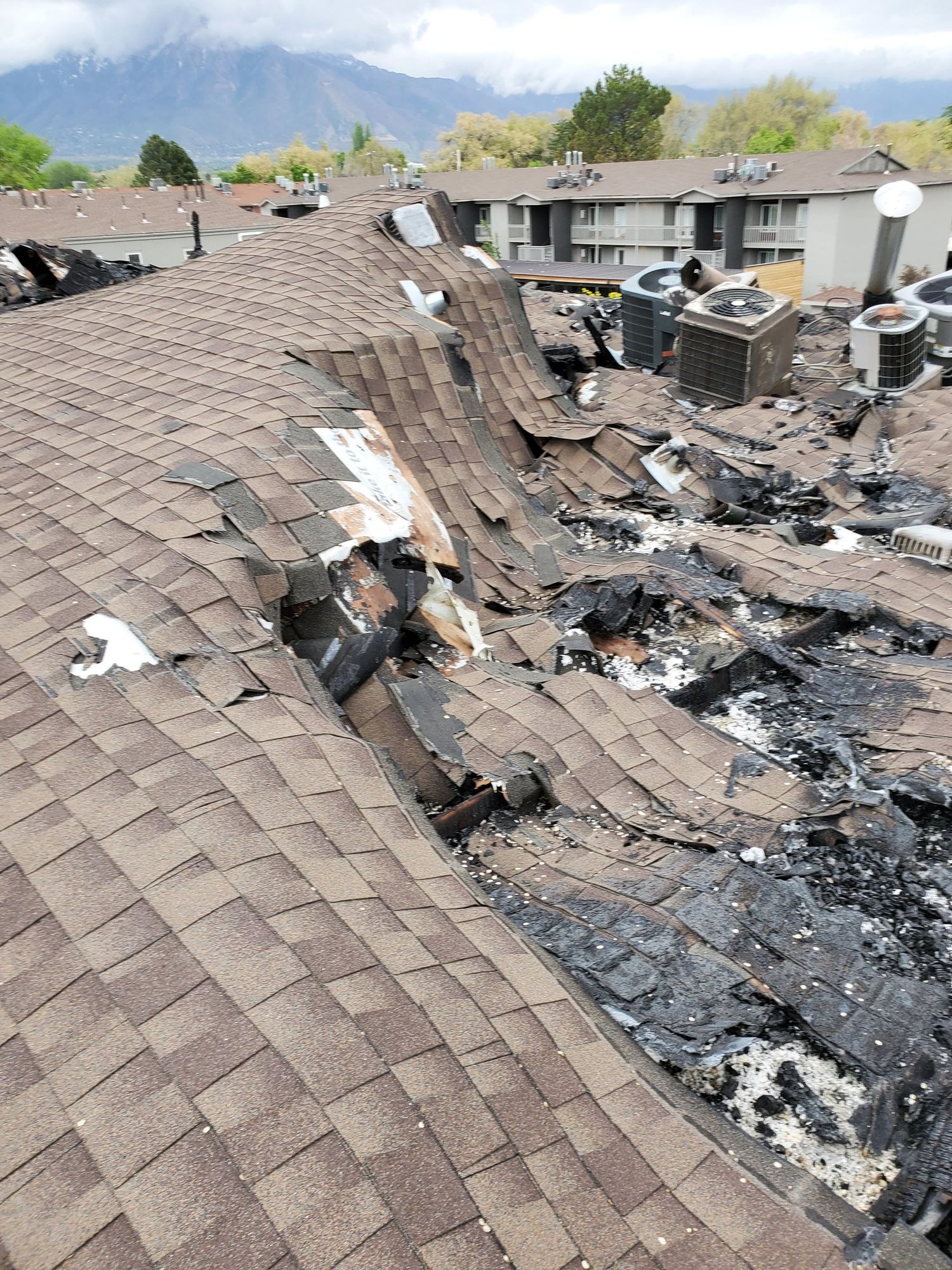 Burned asphalt shingle roof with charred decking and debris next to rooftop air conditioning units, in North Ogden, UT