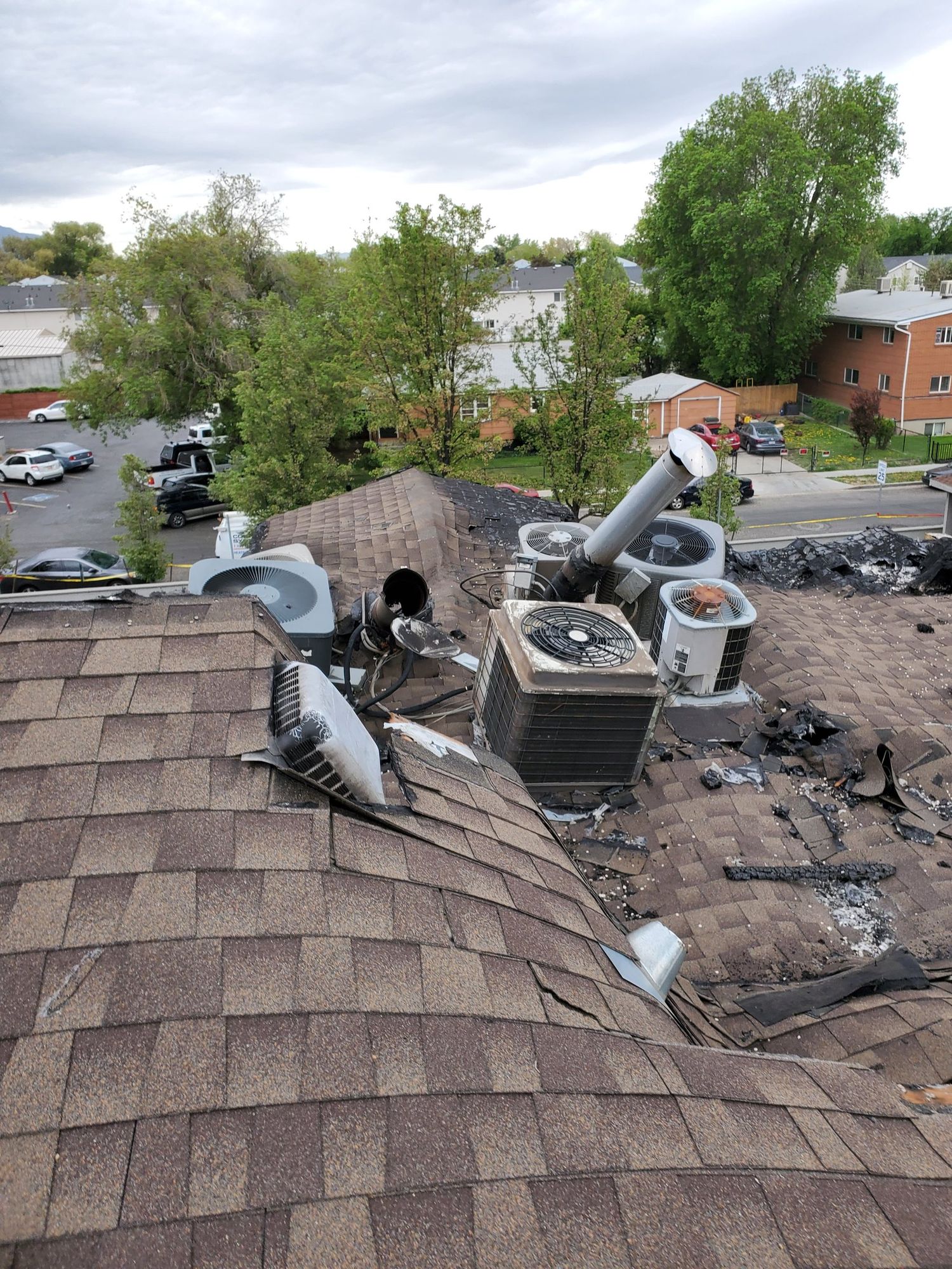Shingle roof with multiple AC condensers, tilted flue pipe, damaged duct and scattered torn black roofing debris, in North Ogden, UT