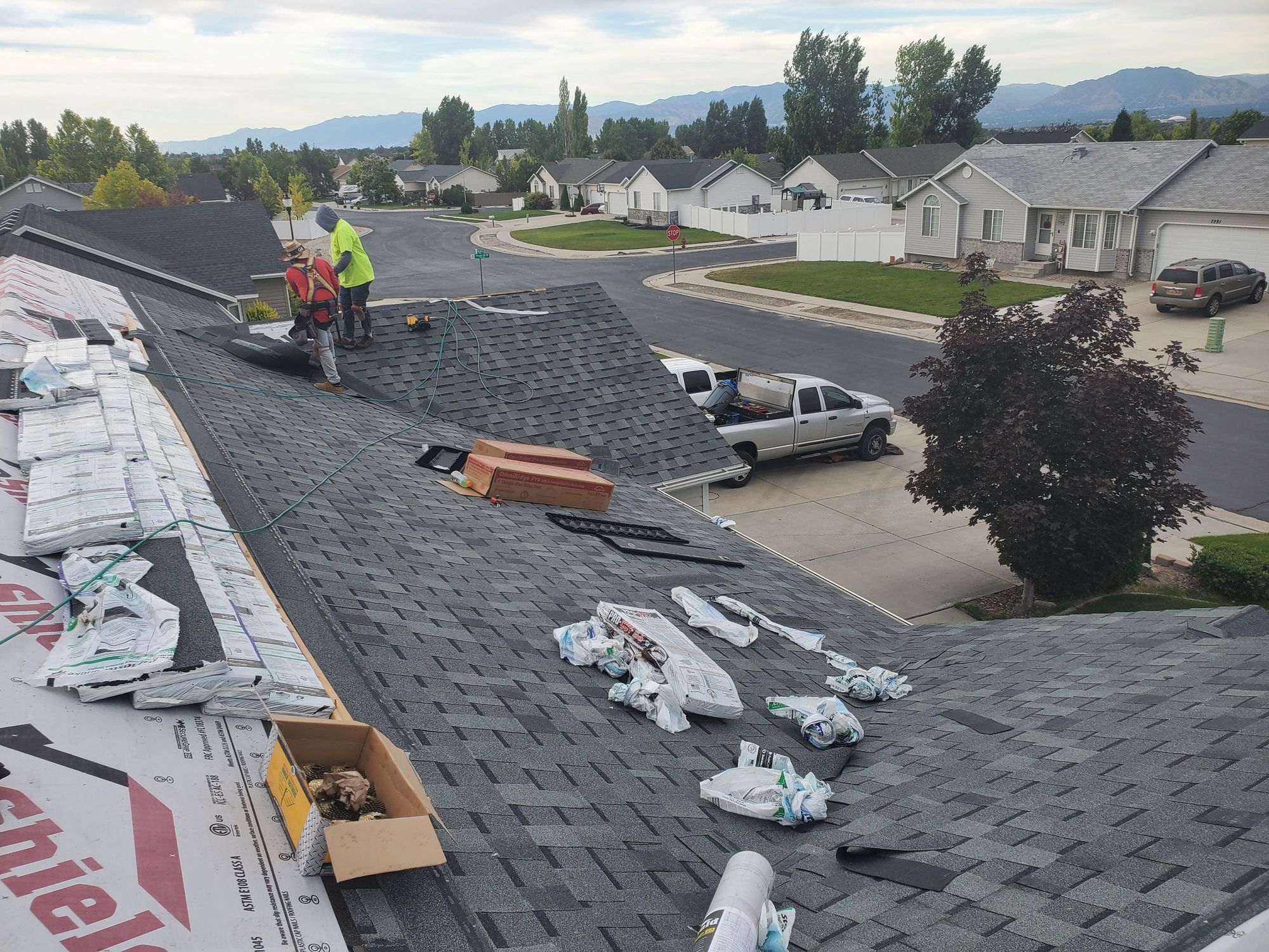 Workers on a pitched roof with new dark asphalt shingles, underlayment, shingle bundles and ridge vent boxes