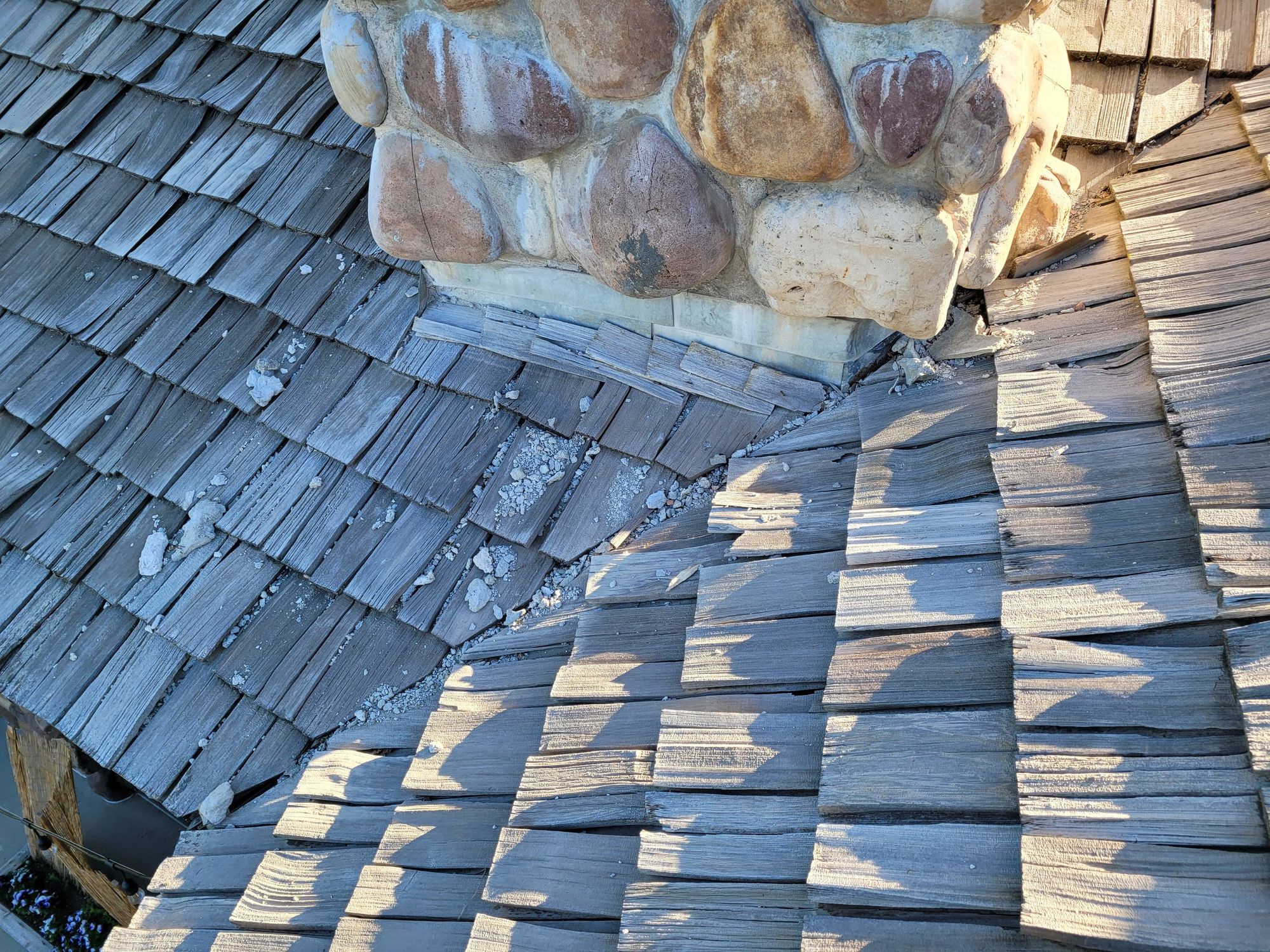 Aged split cedar shakes beside a stone chimney base, with mortar debris scattered in the roof valley, in Murray, UT
