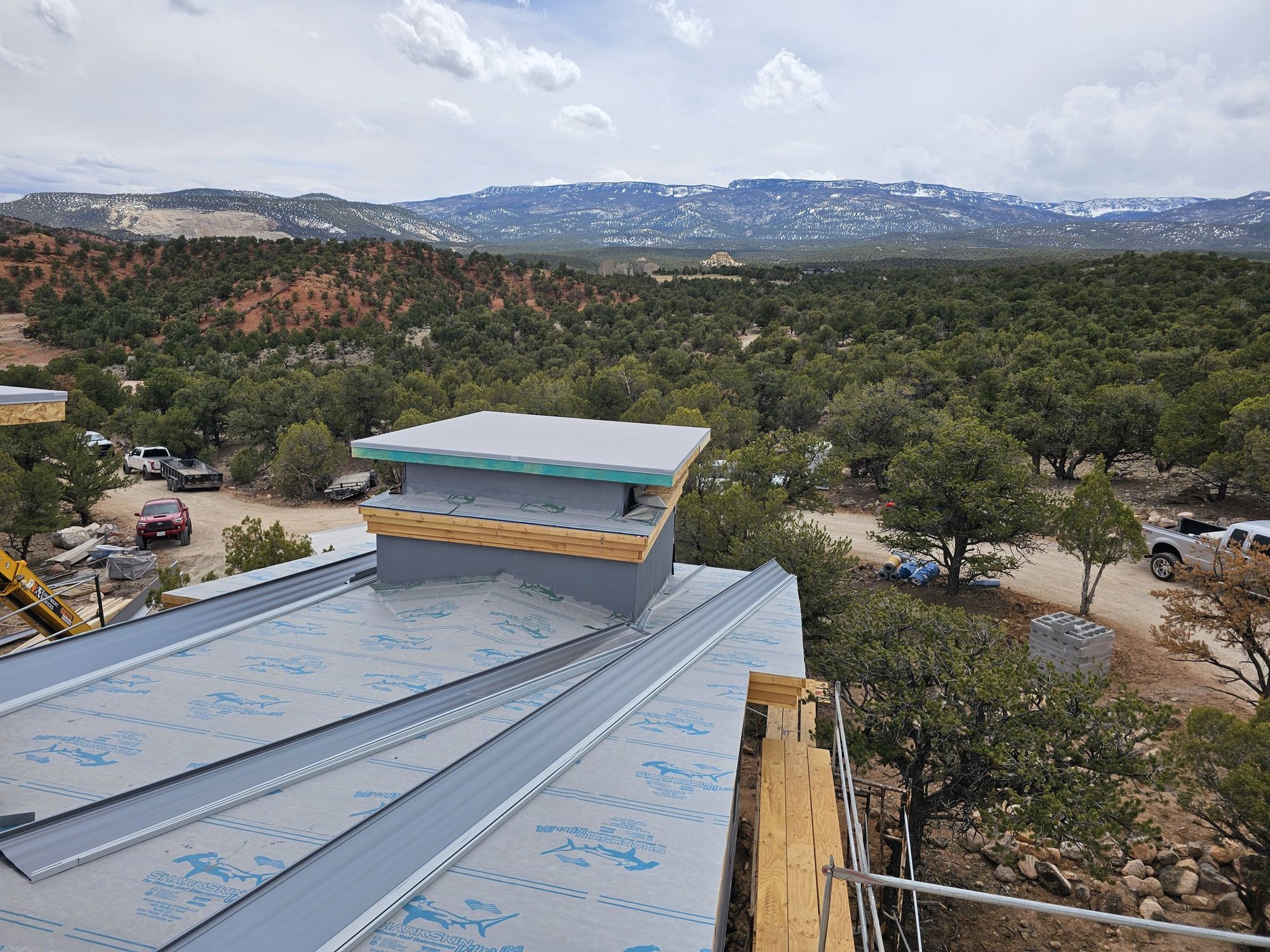 Roof under construction: synthetic underlayment, partly installed standing-seam metal panels, flat-capped tower, wooded hills behind, in Midway, UT