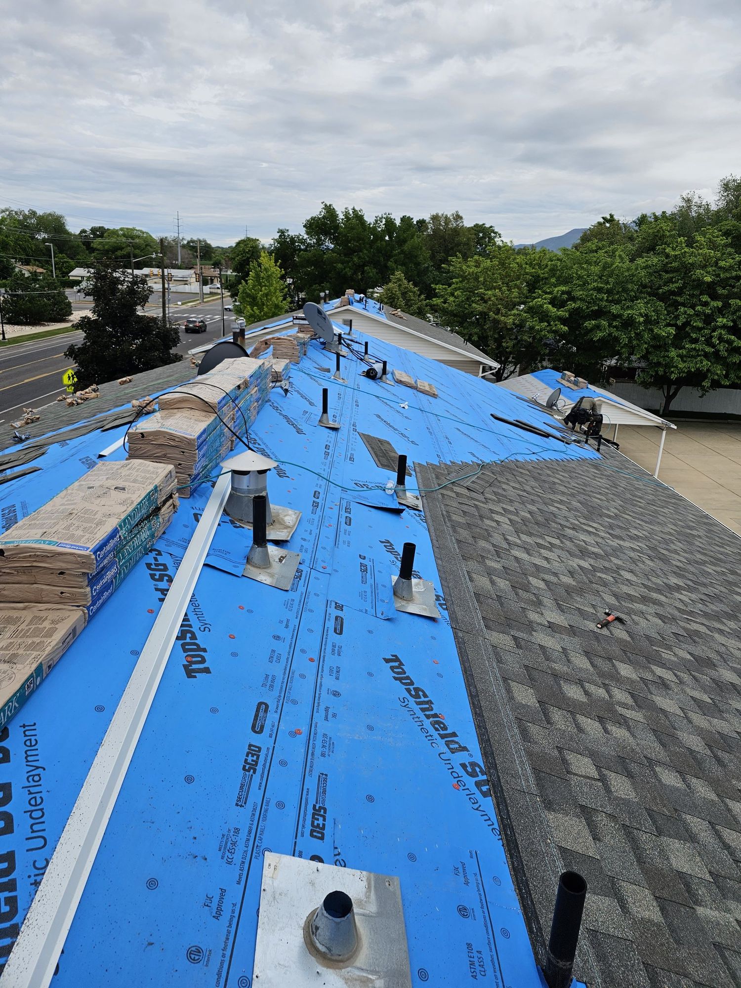 Roof covered in blue synthetic underlayment with new asphalt shingles starting and shingle bundles stacked along the ridge