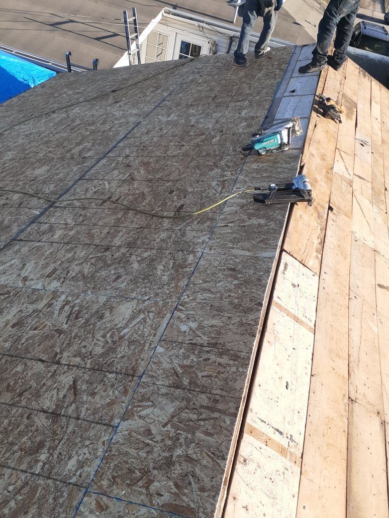 Roof deck with new OSB sheathing beside old plank decking, nail guns, workers' legs at ridge