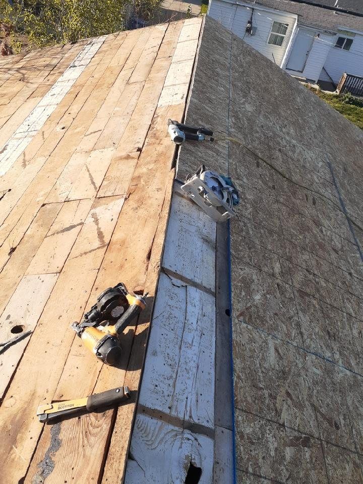 Bare roof deck with old boards, new OSB, metal valley flashing, nail guns and hammer
