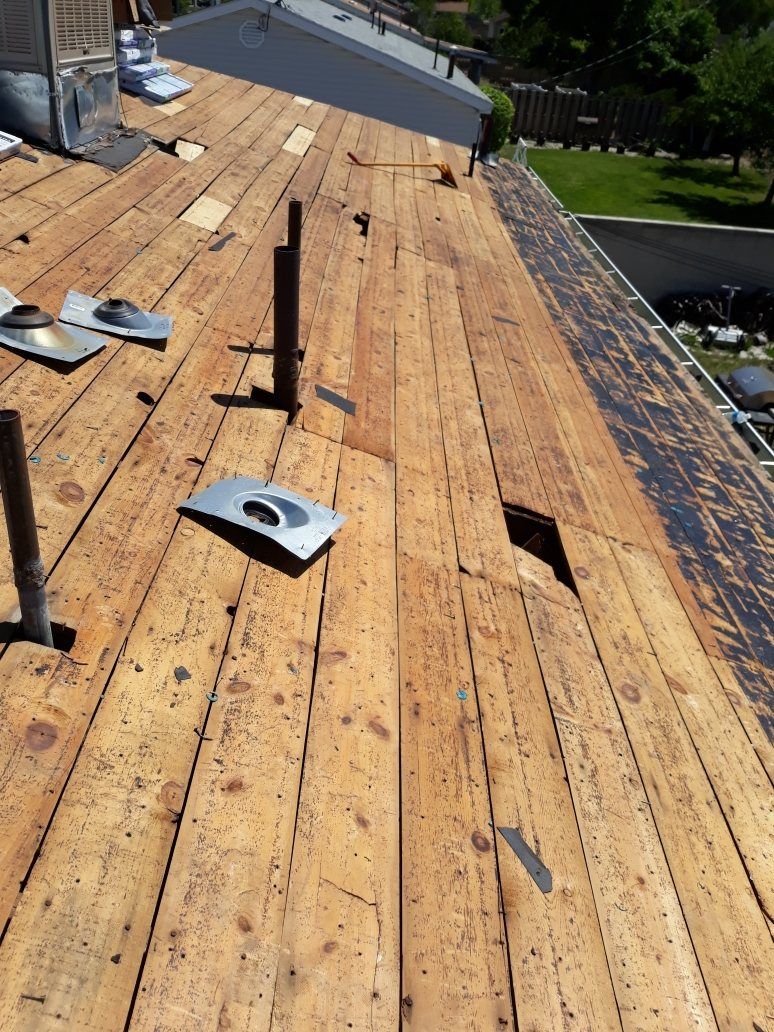 Bare wood plank roof decking after tear-off with loose pipe flashings, vent pipes and an open hole, in West Valley City, UT