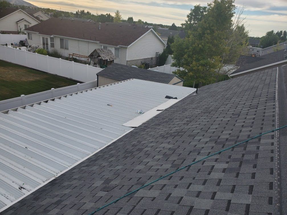 Dark asphalt shingle roof plane meeting white ribbed metal panel roof, suburban homes and vinyl fence behind