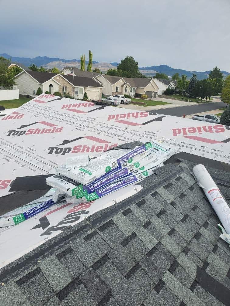 Partly shingled roof with white underlayment, staged shingle bundles, suburban homes and mountains behind