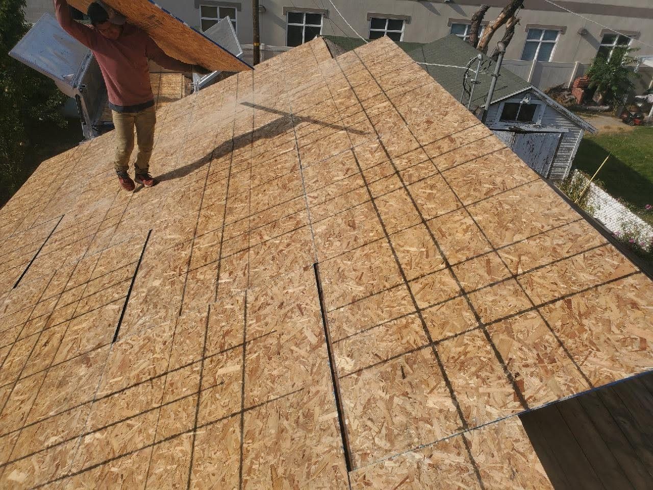 Worker carrying an OSB panel on a hip roof covered in fresh chalk-lined plywood sheathing