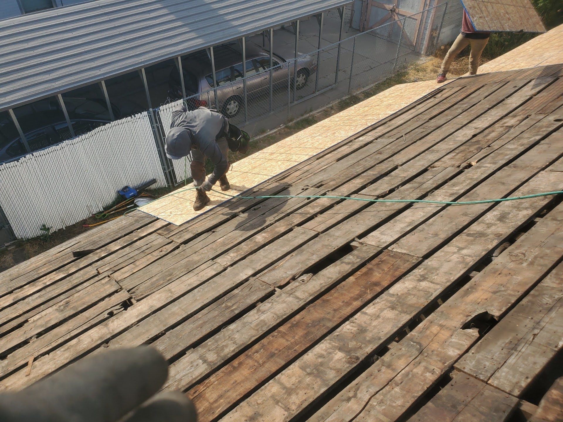 Two workers on a stripped roof of weathered board decking, with new OSB sheathing panels laid along the upper slope, in Riverton, UT