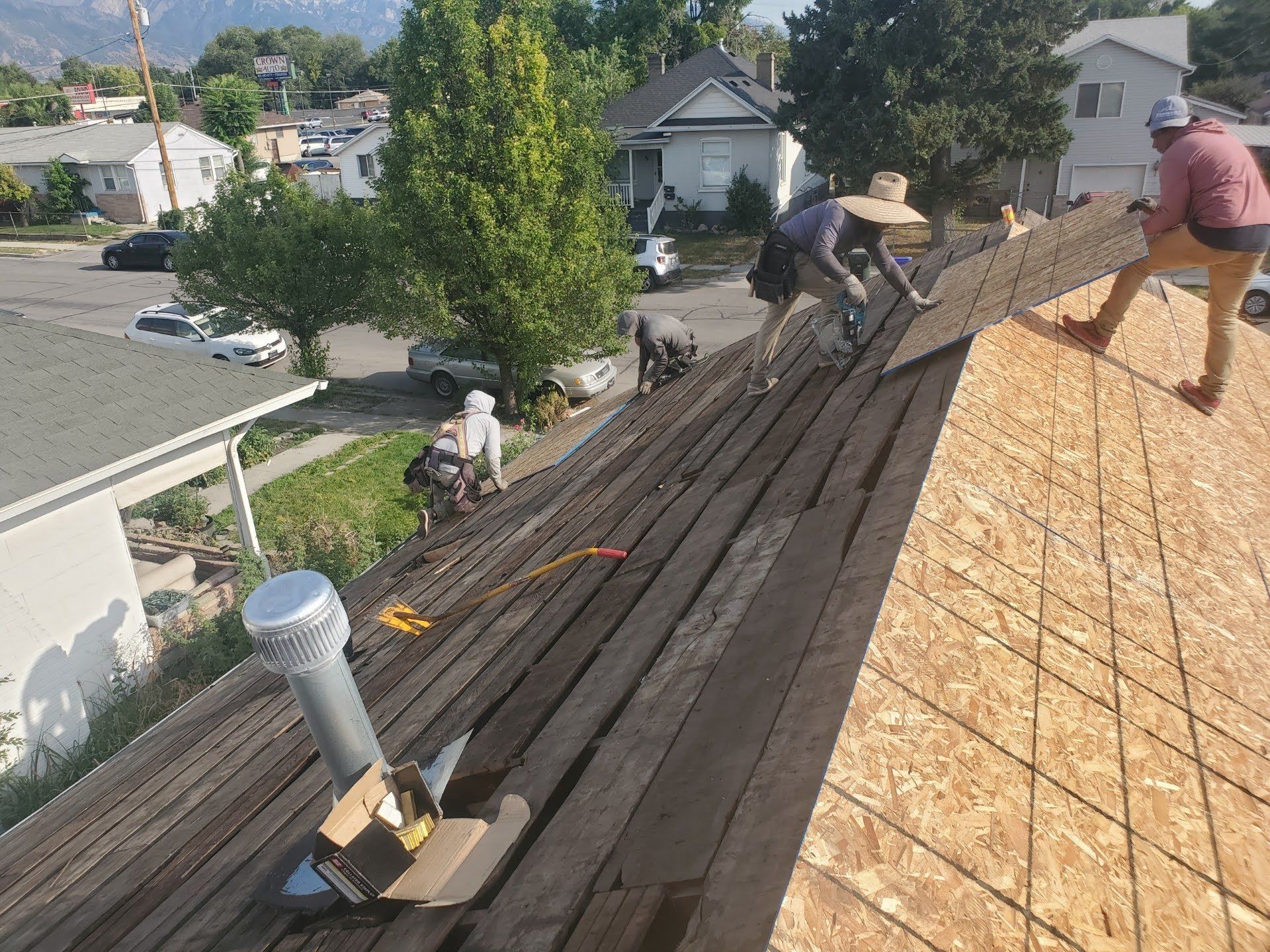 Workers on a stripped roof laying new OSB sheathing over old weathered plank decking