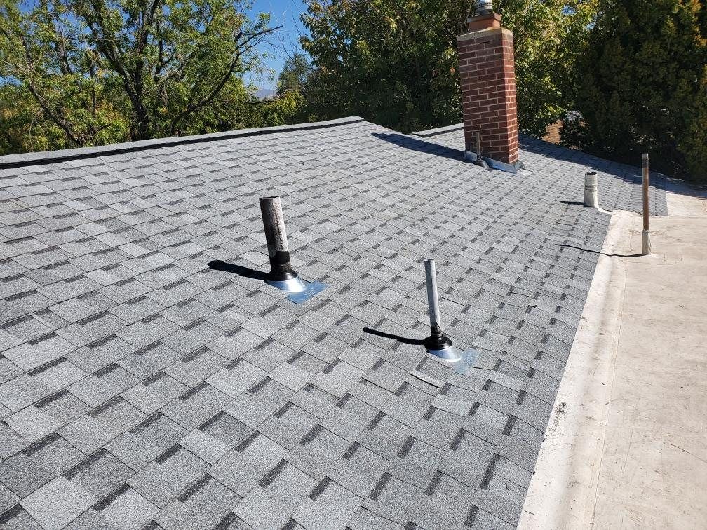 Gray asphalt shingle roof with two vent pipe boots, red brick chimney and flat section beside it
