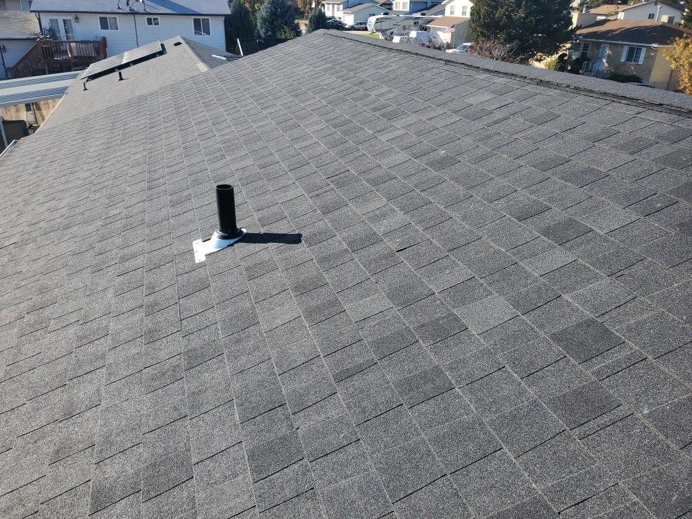 Gray asphalt shingle roof plane with black pipe vent in white flashing, houses in background