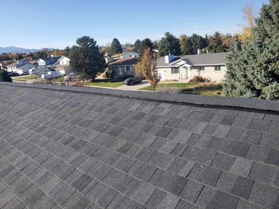 Weathered gray asphalt shingle roof seen from the ridge, with suburban houses and mountains beyond, in Park City, UT
