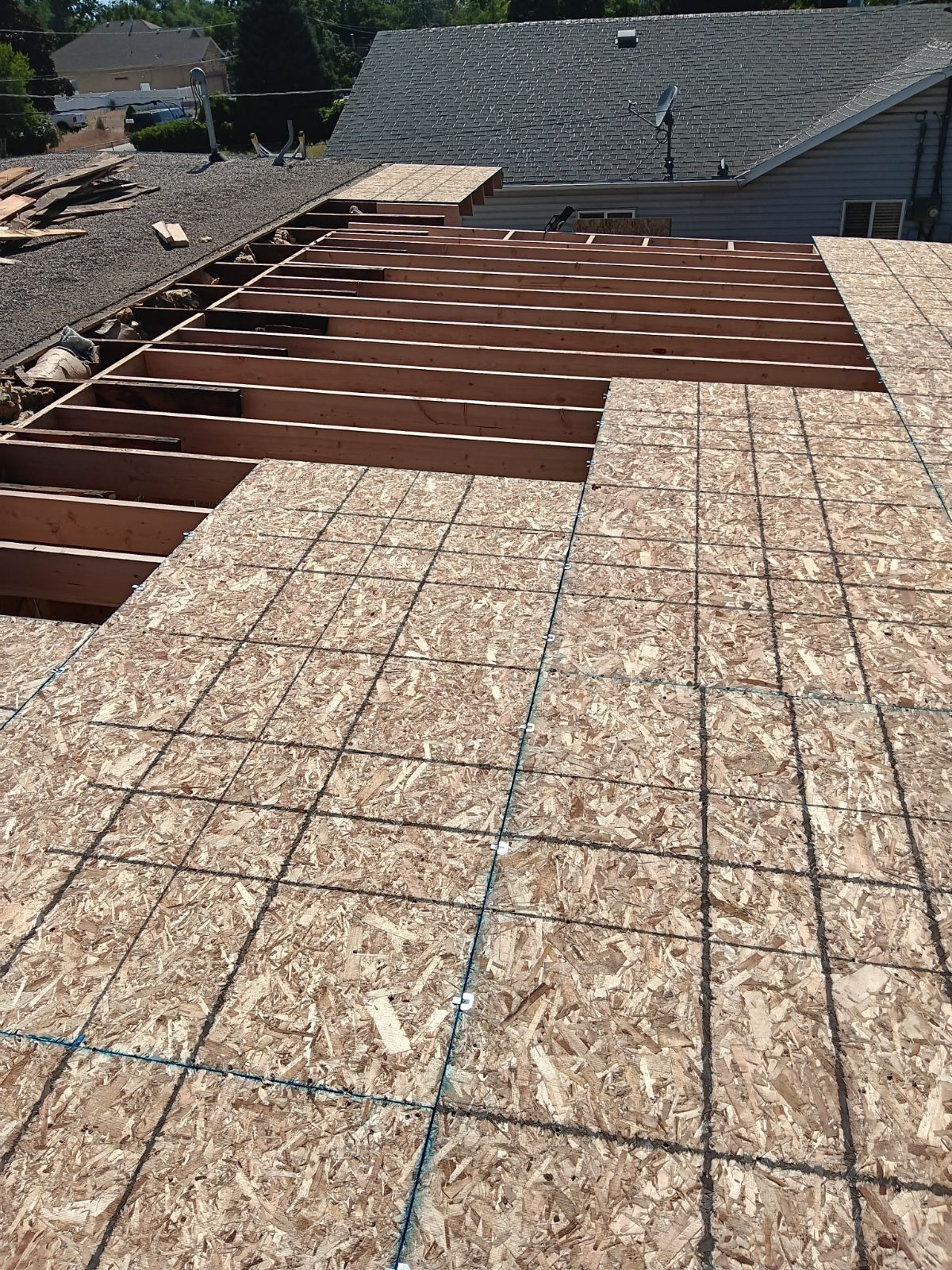 Partially sheathed low-slope roof with new rafters, chalk-lined OSB panels, and a shingled house behind