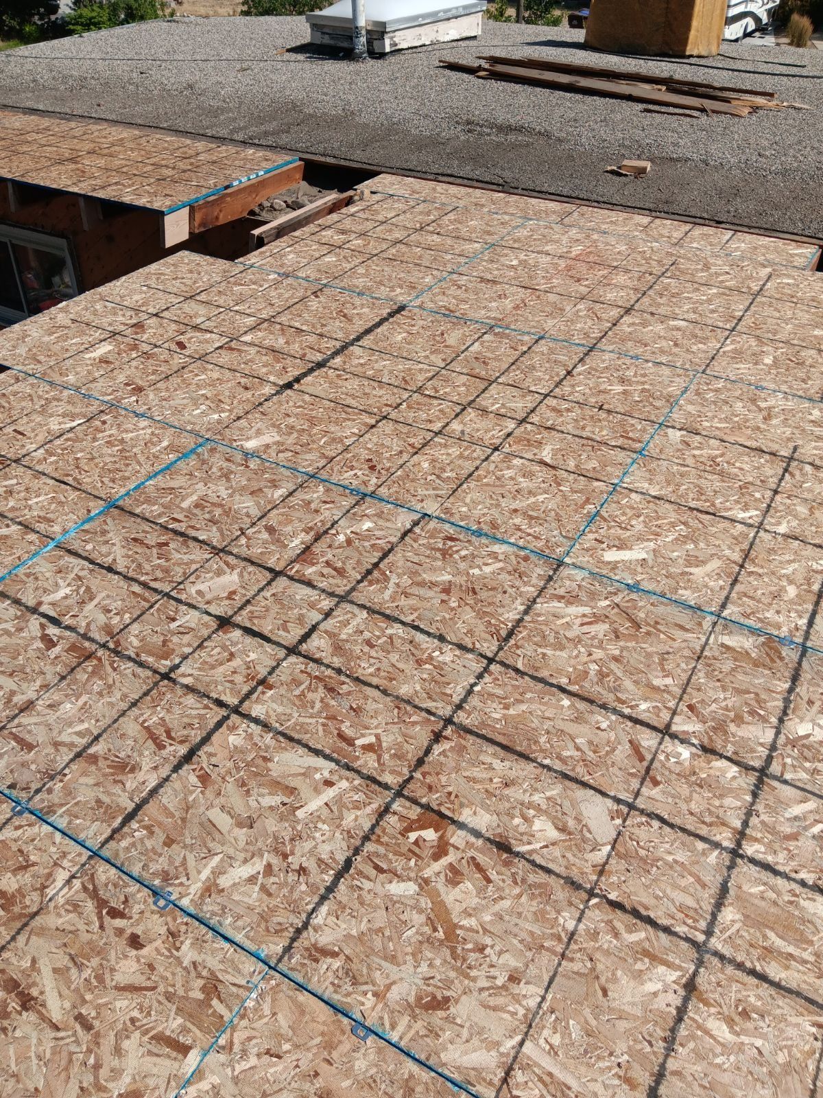 Newly sheathed OSB roof deck marked with chalk lines beside an older gravel roof with scrap lumber