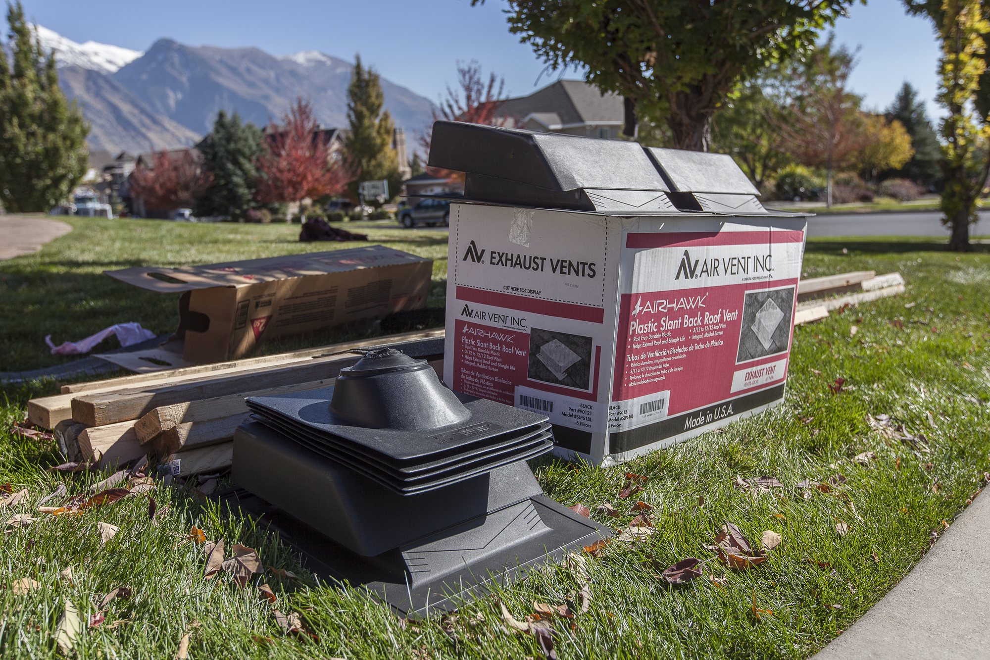 Cartons of AirHawk plastic slant-back roof vents and loose black vents staged on grass, mountains behind