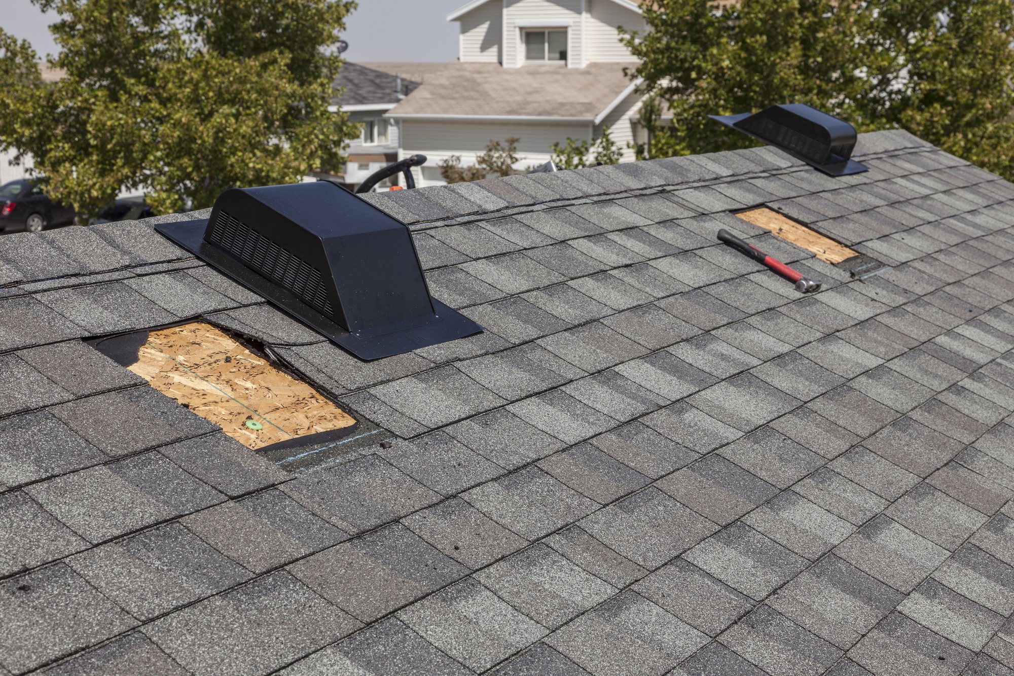 Gray shingle roof with black box vent installed and a second vent opening cut to bare decking